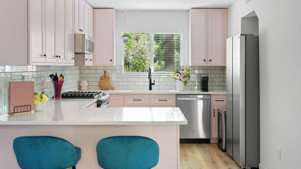 Una cocina moderna con armarios rosas, encimera blanca y electrodomésticos de acero inoxidable.