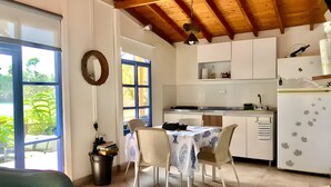 A modern kitchen with white cabinets, a dining table with chairs, and a view of greenery outside. - La Comarca Guatape (El Peñol)