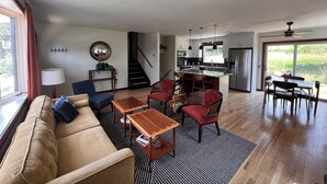 En rummelig opholdsstue med sofa, sofabord og stole, et køkken med bar samt en trappe til et andet niveau.