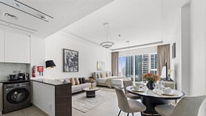 A modern apartment with a kitchen, dining area, and living room. It features a large window with a city view, a washing machine, and a dining table set for four. - ME DO RE residence (Dubai)