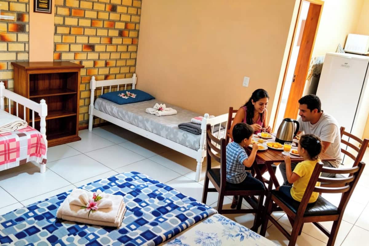 A family dining in a room with a brick wall, a small bed, a wooden cabinet, and a tiled floor.