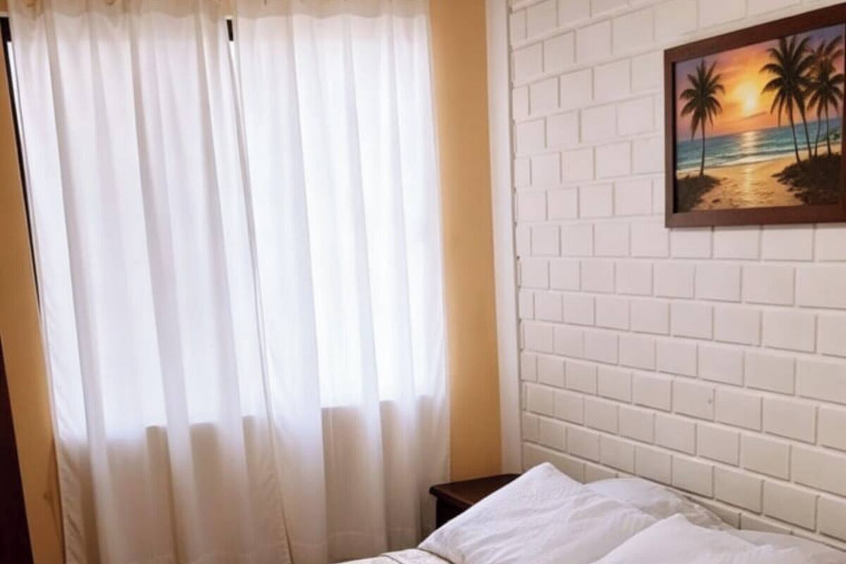 A bed with a patterned bedspread, a rolled towel, and a nightstand with a lamp.