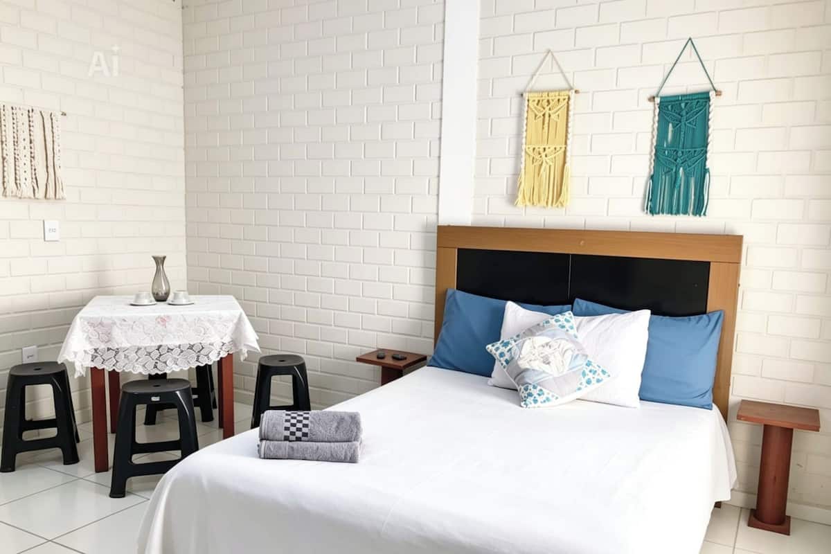 A bedroom with a bed, two nightstands, a table with chairs, and macramé wall hangings.