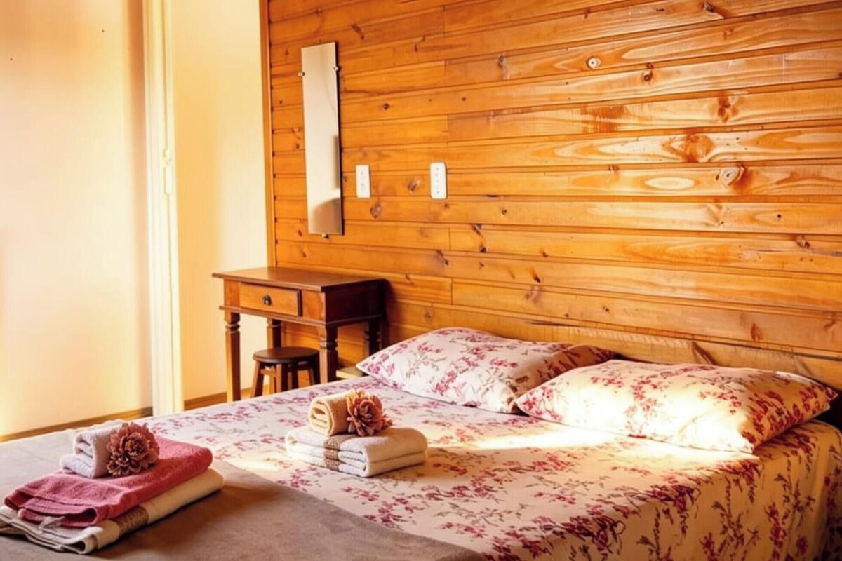 A wooden-paneled room with a bed, a small table, and a TV on the wall.