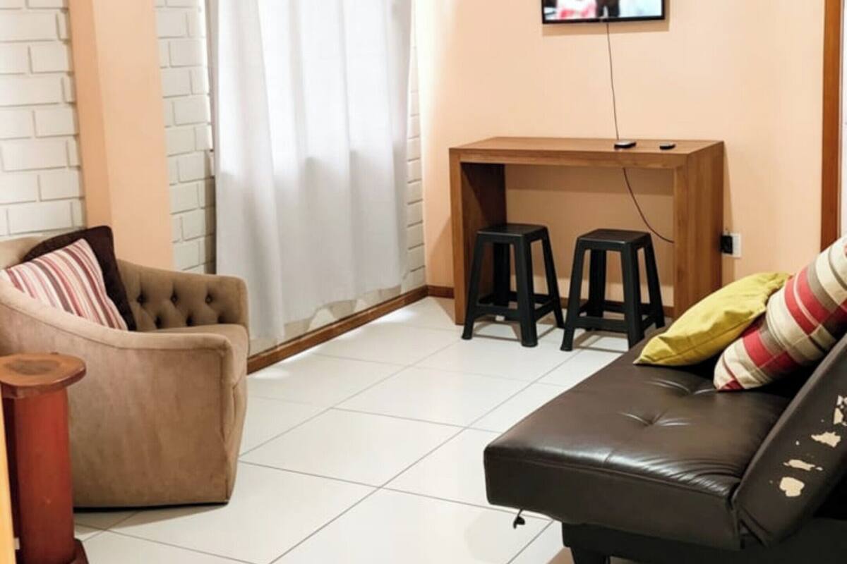 A living room with a sofa, a chair, a small table with stools, a television, and a brick wall.
