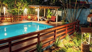 Une piscine dotée d’une terrasse en bois et d’une rambarde, entourée d’une végétation luxuriante et de palmiers.