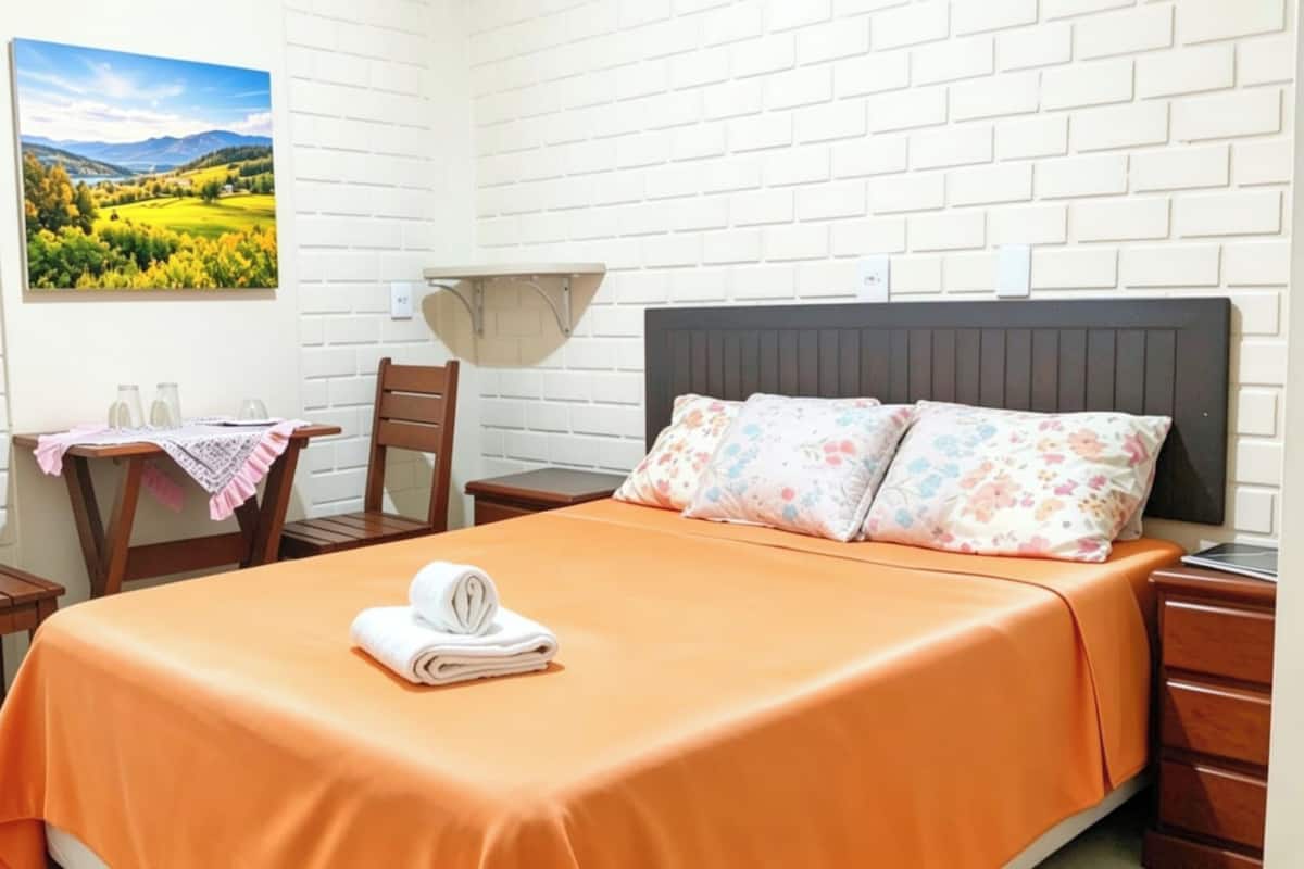 A hotel room with a bed, a table with chairs, a picture on the wall, and a nightstand.