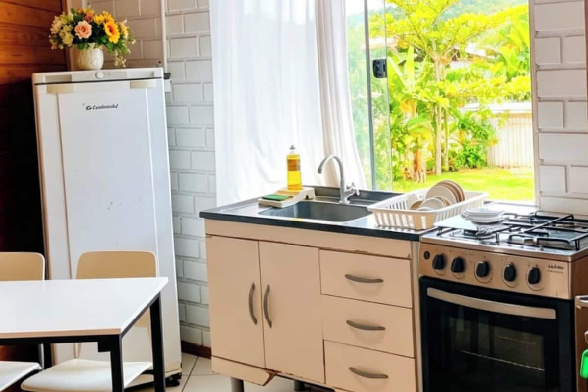 A kitchen with a white refrigerator, a sink, a stove, and a window with a view of greenery.
