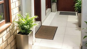 Un couloir avec une porte en bois, une plante en pot et un sol carrelé.
