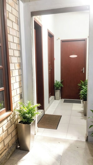 A hallway with a wooden door, a potted plant, and a tiled floor. - Pousada Aurema (Imbituba)