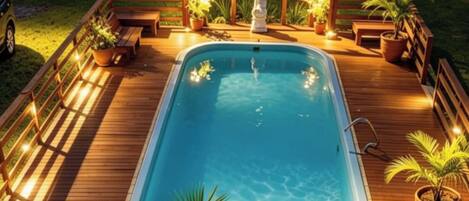 Ein Schwimmbecken mit Holzterrasse, umgeben von Blumentöpfen und Bänken.