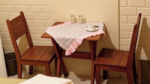 Une pièce avec une table en bois, deux chaises, un tableau encadré représentant une plage et une petite table sur laquelle se trouvent une tasse et des salières.