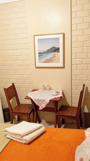 A room with a wooden table, two chairs, a framed picture of a beach, and a small table with a cup and salt shakers. - Pousada Aurema (Imbituba)