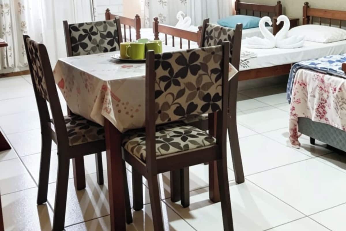 A room with a dining table, chairs, a bed, and an air conditioning unit.