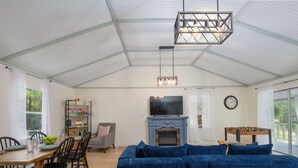 A spacious room with a large blue sectional sofa, a dining table with chairs, a fireplace, and a television mounted above it.