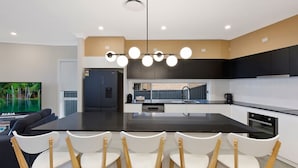 Cozinha moderna com ilha central, cadeiras brancas e televisão de tela plana.