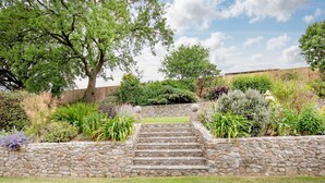 A stone staircase leading up to a wooden fence, surrounded by lush greenery and various plants. - Sutton Barton Farmhouse (Honiton)