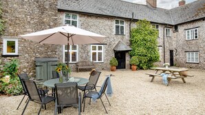 A stone building with a patio area featuring a round table, chairs, a picnic table, and a large umbrella. - Sutton Barton Farmhouse (Honiton)