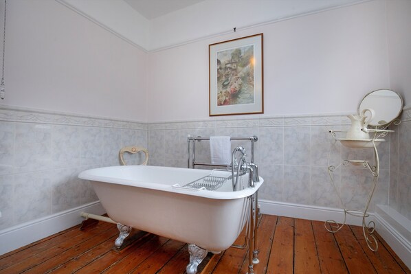 Une salle de bain avec une baignoire sur pieds, un porte-serviettes, un miroir posé sur un support et un tableau encadré accroché au mur.