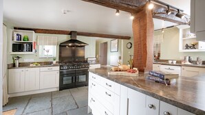 A modern kitchen with white cabinetry, a large island, a built-in stove, and a stone floor. - Sutton Barton Farmhouse (Honiton)