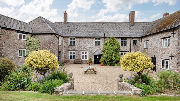 A stone building with a courtyard, a bench, and potted plants. - Sutton Barton Farmhouse (Honiton)
