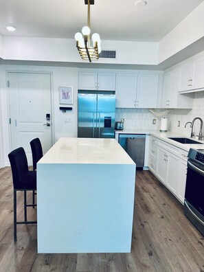 A modern kitchen with a central island, stainless steel appliances, white cabinetry, and a black countertop. - Modern and Updated 2-bed/2-bath Condo in Silicon Valley! (Los Angeles)