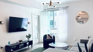 Ein modernes Wohnzimmer mit Flachbildfernseher, rundem Spiegel, Deckenventilator und großem Fenster mit Vorhängen.