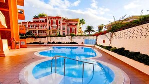Una piscina con borde de azulejos, rodeada por un muro bajo y un edificio con balcones.