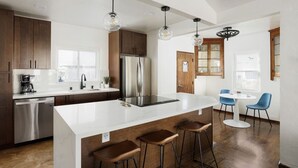 A modern kitchen with a large island, bar stools, and a dining area with chairs. - Ocean Beach Spanish Gem | Walk to beach pier shops (San Diego)