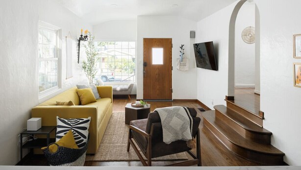 A living room with a yellow sofa, a wooden chair, a coffee table, and a staircase leading to an upper floor. - Ocean Beach Spanish Gem | Walk to beach pier shops (San Diego)
