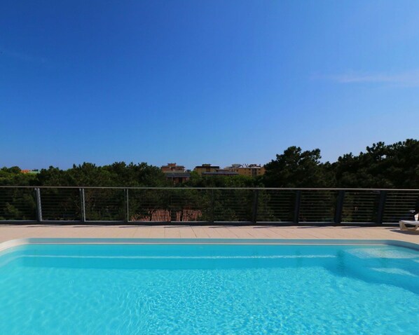 A clear blue swimming pool with a view of buildings and trees in the background.