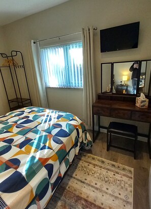 Un dormitorio con cama, escritorio, silla, televisor y ventana con cortinas.