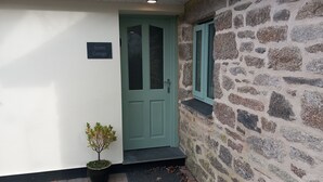 L'ingresso di un cottage con una porta verde, una pianta in vaso e un muro in pietra.