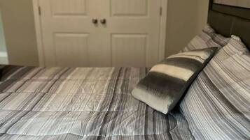 Ein Bett mit gestreifter Bettwäsche und zwei Kissen, eine geschlossene Tür im Hintergrund und ein Kopfteil auf der rechten Seite.