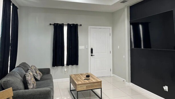 Un salon moderne avec un canapé gris, une table basse en bois, un ventilateur de plafond et une porte coulissante noire.
