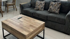 Un salon moderne avec un canapé gris, deux coussins décoratifs à motifs, une table basse en bois et un tableau encadré accroché au mur.
