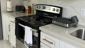 Une cuisine moderne avec des meubles blancs, une cuisinière noire, un four à micro-ondes et un évier en acier inoxydable.