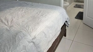 Une chambre à coucher avec un lit, un téléviseur fixé au mur et une salle de bain visible à travers une porte ouverte.