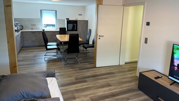 A modern apartment with a dining area, kitchenette, and a TV in the living room.