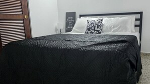 A bedroom with a bed, a black headboard, a white wall, a door with blinds, and a motivational quote on the wall.