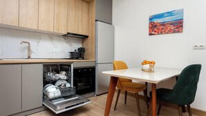 Une cuisine compacte avec des meubles en bois, un lave-vaisselle encastré et un coin repas comprenant une table blanche et deux chaises.
