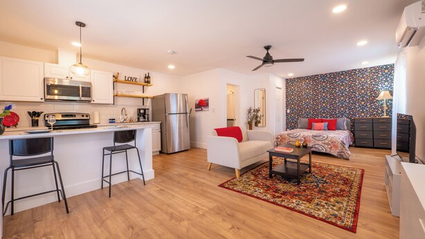 Eine moderne Wohnung mit Küche, Essbereich und Wohnzimmer. Sie beinhaltet einen Kühlschrank, eine Mikrowelle und eine Kaffeemaschine. Es gibt ein Sofa und einen kleinen Tisch mit Teppich.