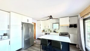 Uma cozinha moderna com armários brancos, uma geladeira de aço inoxidável, forno embutido e um espaço de bar com dois bancos.