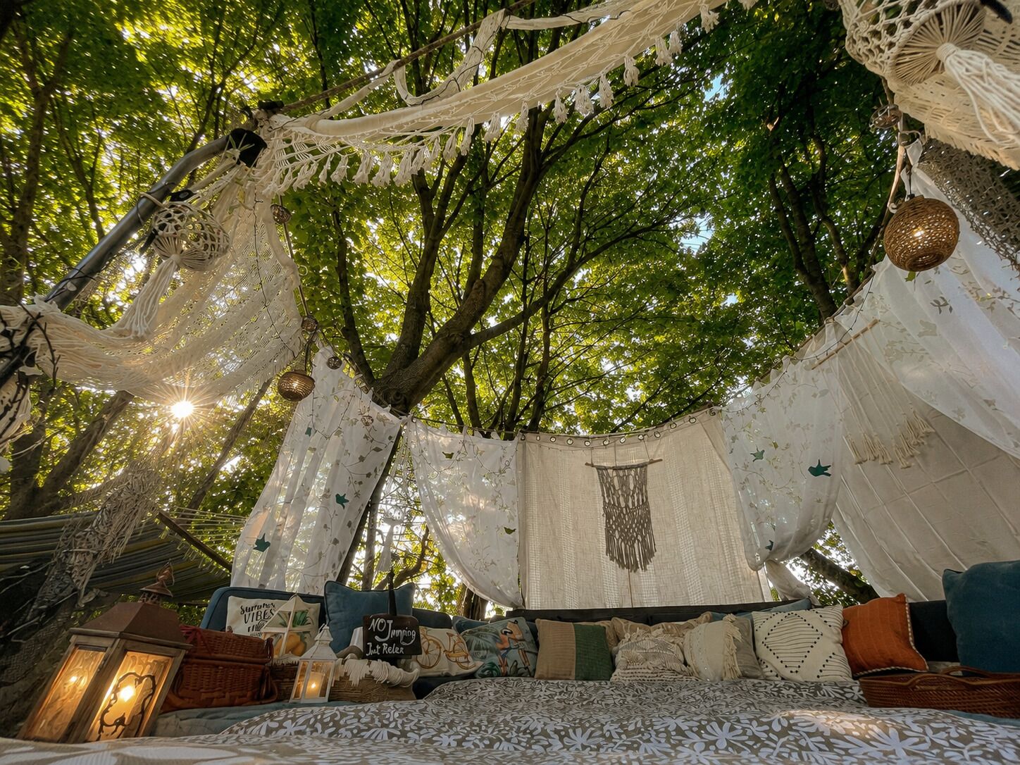 Un llit d'hamaca sota un arbre, decorat amb penjolls de macramé i un dosser.