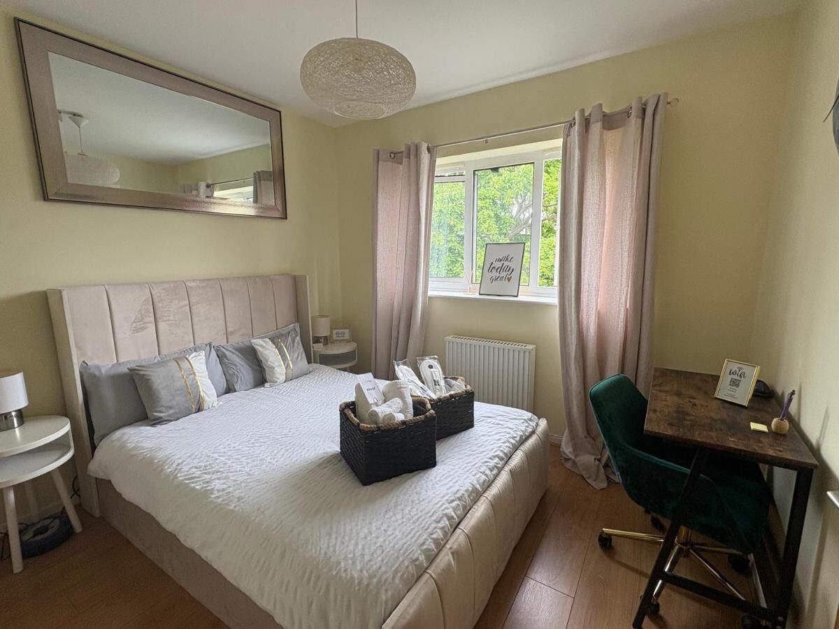 A hotel room with a bed, bedside table, chair, desk, and window with curtains.