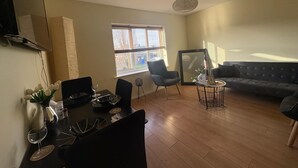 En stue med spiseplads, sofa, fjernsyn og et vindue med persienner.
