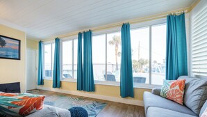 Ein Zimmer mit großem Fenster, einer Couch, einem Sessel und einem gemusterten Teppich.
