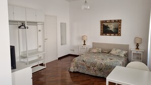A bedroom with a bed, bedside tables, a wardrobe, a desk, and a hanging light fixture.
