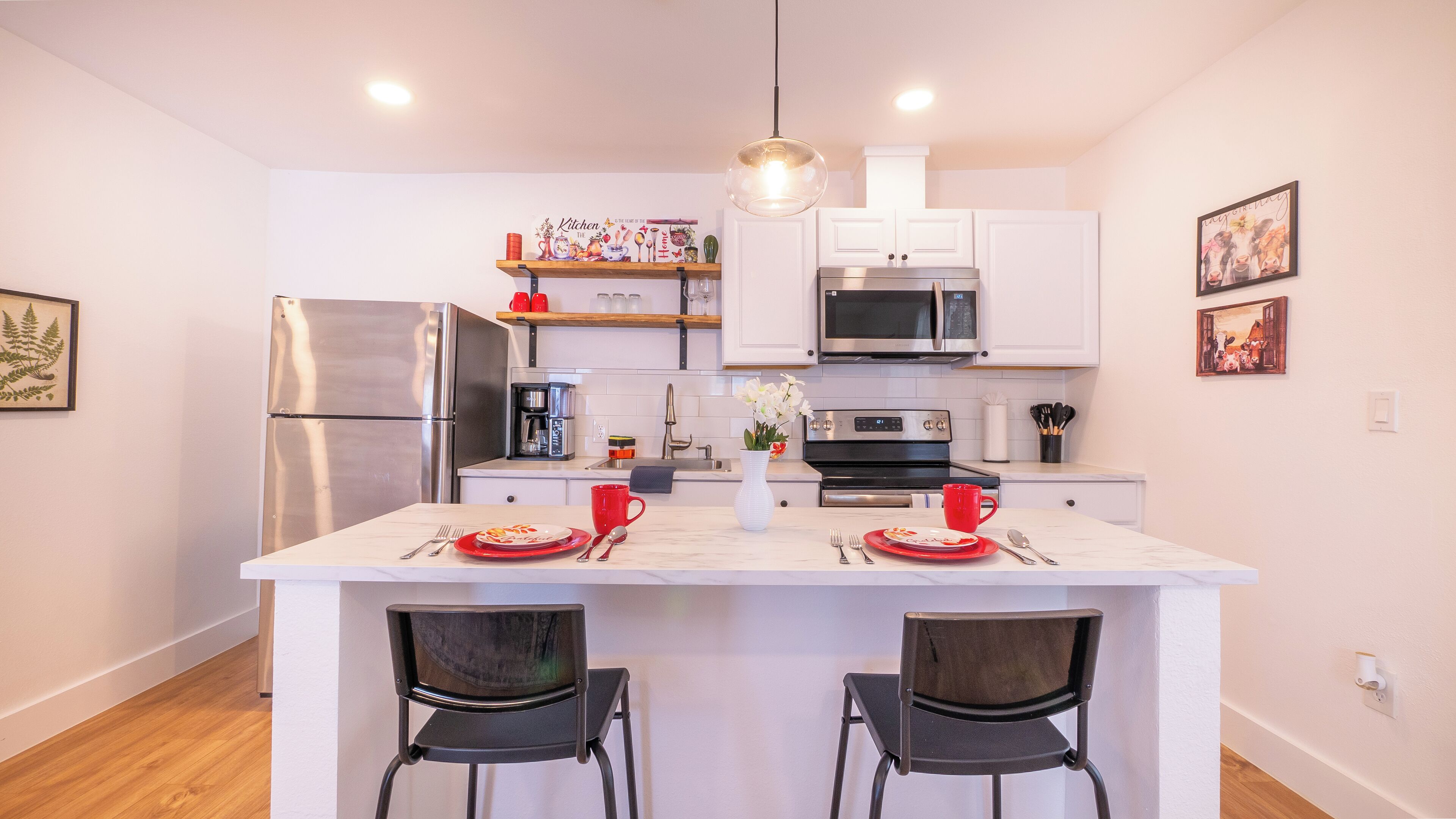 Een moderne keuken met witte kasten, roestvrijstalen apparatuur en een centraal kookeiland met twee stoelen.