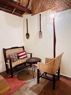 Un rincón acogedor con un banco de madera, una silla de mimbre, una mesita redonda y detalles decorativos rústicos en la pared.